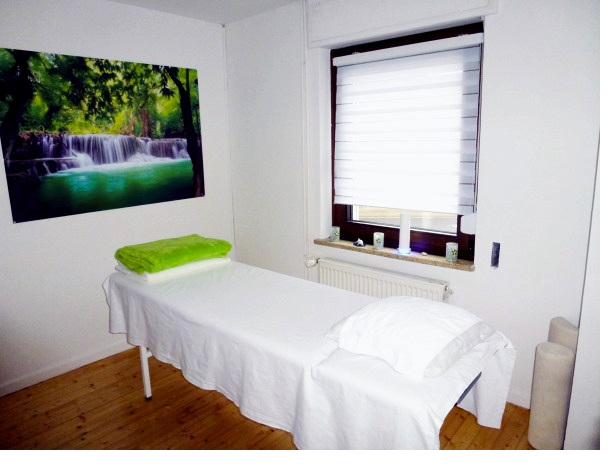 Behandlungsliege am Fenster, an der Wand ein Bild mit Wasserfall